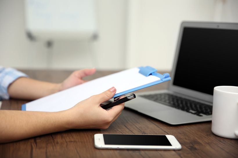 Work concept clipboard in woman hands laptop and cup of tea on wooden table.