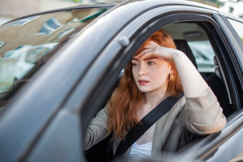 Nervous female driver sits at wheel has worried expression.