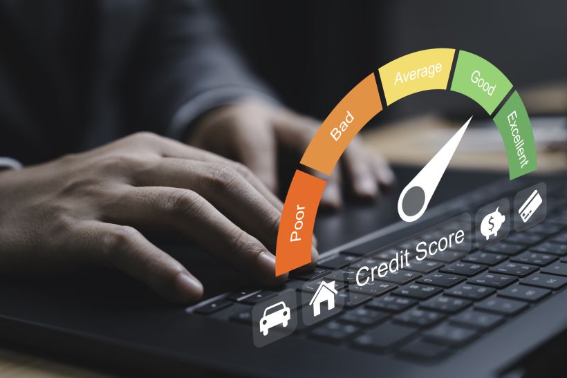 Closeup of hand typing on a laptop with a credit score gauge displayed the gauge indicates varying levels of credit quality.