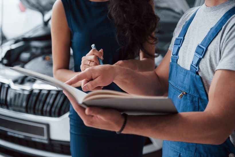 Woman in the auto salon with employee in blue uniform taking her repaired car back.