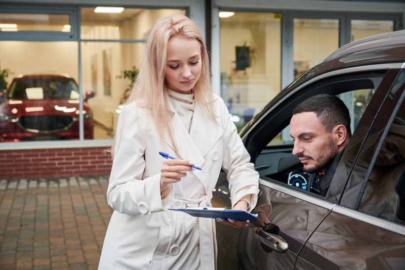 Woman salesperson asking to sign some documents at car dealership.