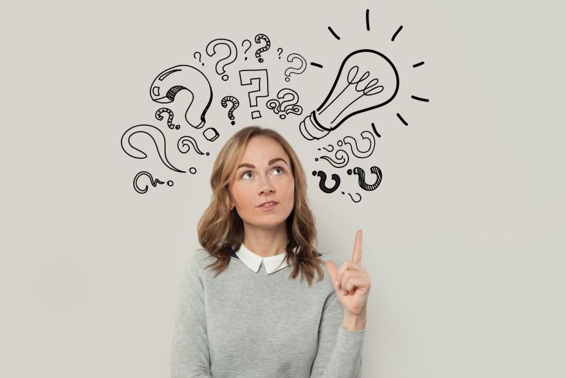 A nice woman in a gray sweater has an idea and points to a light bulb on a gray background.