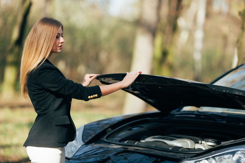 A woman waits for assistance near her car broken down on the road side.
