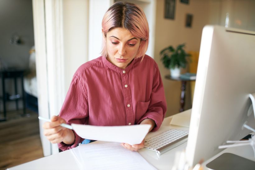 Young female with pinkish hair reading car documents.