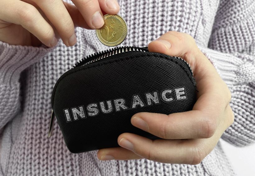 Woman's hand putting coin in black wallet with word insurance.