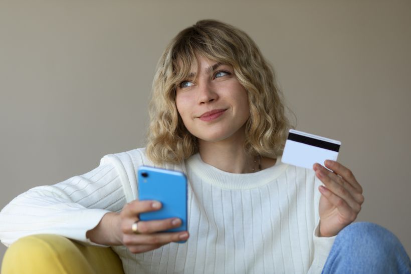 Vista frontal de una mujer utilizando un dispositivo electr&oacute;nico y una tarjeta de cr&eacute;dito.