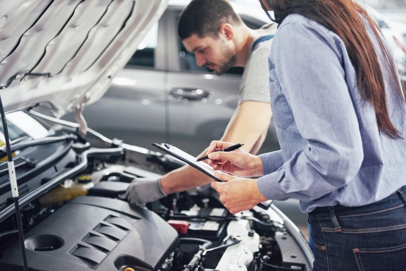 Un mec&aacute;nico y una clienta miran el cap&oacute; del coche y hablan sobre las reparaciones.