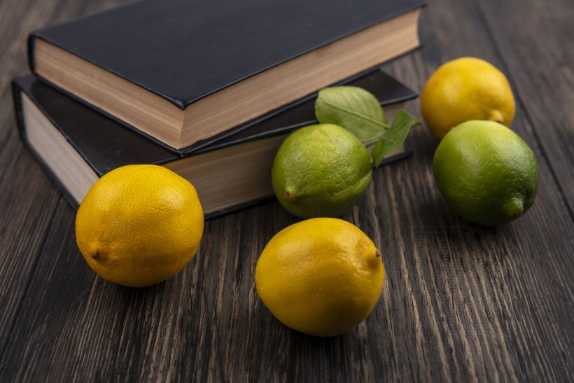 Vista frontal de limones con limas y libros sobre fondo de madera.