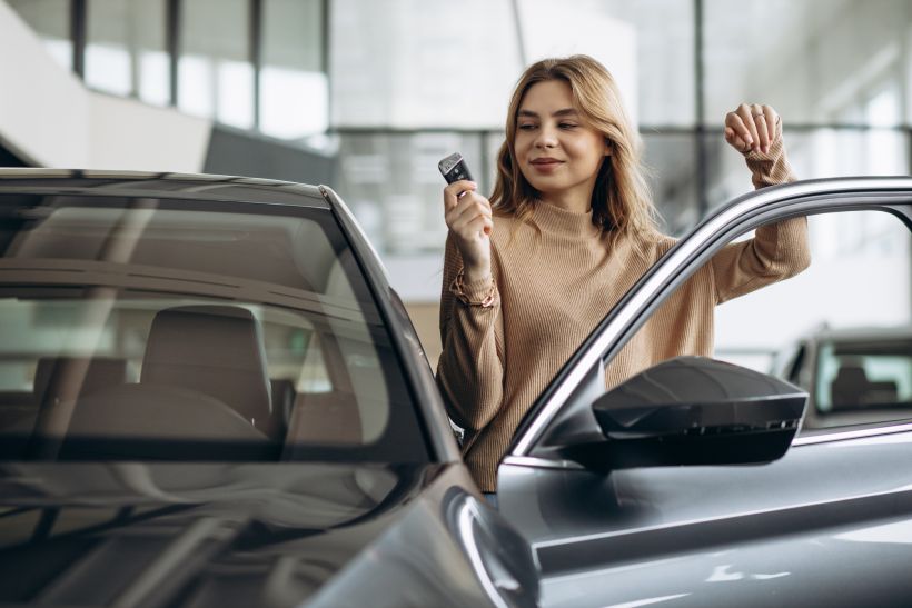 Mujer sosteniendo las llaves junto a su coche nuevo.