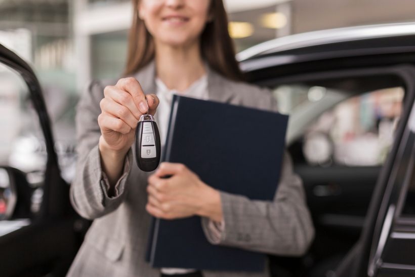 Manos femeninas sosteniendo una carpeta y las llaves del coche.