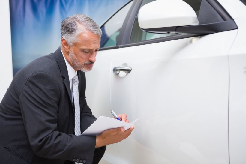 Empresario mirando un coche mientras escribe en un portapapeles.