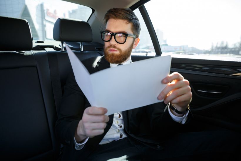 Empresario con documentos conduciendo en el asiento trasero del coche.