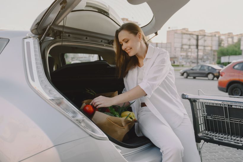 Una mujer sonriente está sentada en el maletero de su coche con la compra.