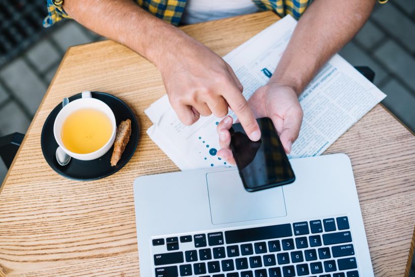 Hombre sentado a la mesa con caf&eacute; y dispositivos electr&oacute;nicos buscando informaci&oacute;n sobre coches.