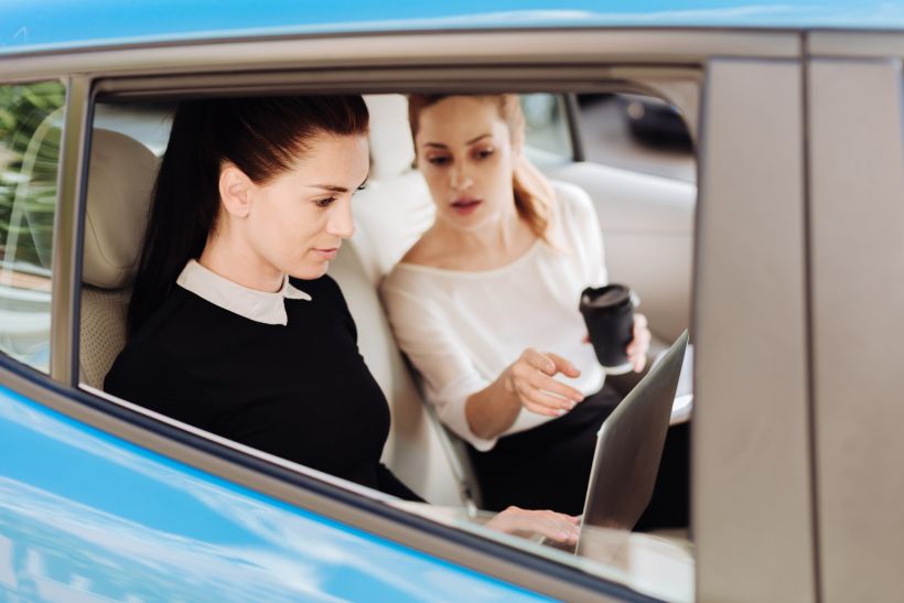 Una agradable mujer de negocios sentada en el coche con su colega y señalando la pantalla del ordenador portátil.