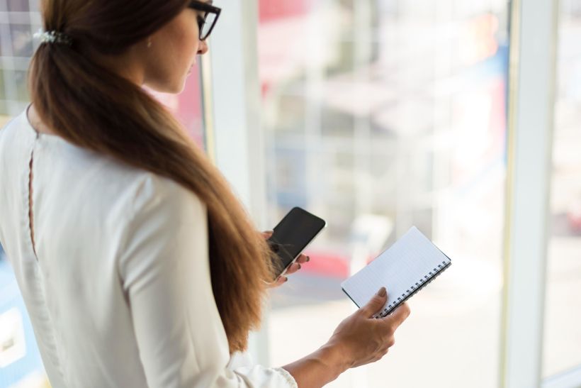 Vista lateral de una mujer de negocios con un smartphone y un cuaderno.