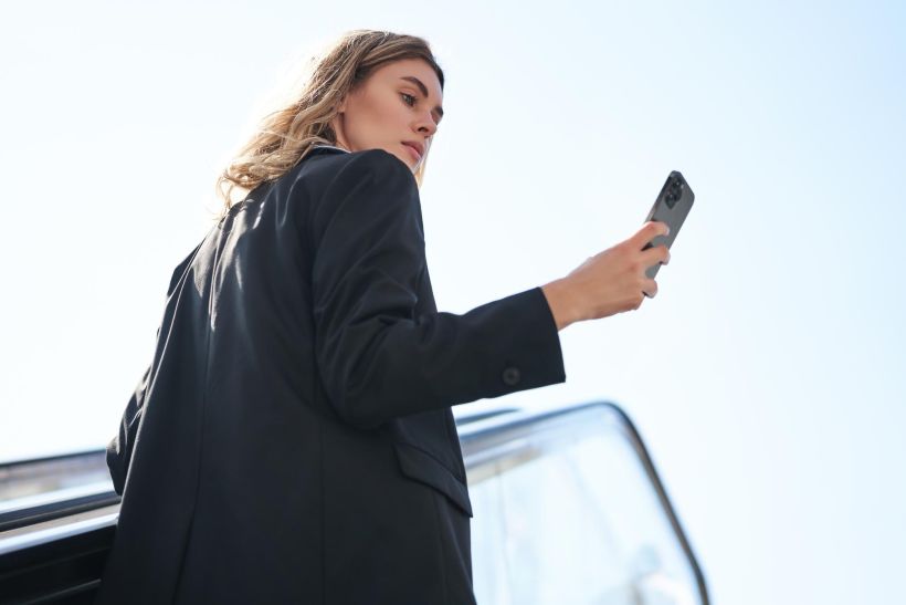 Una exitosa mujer de negocios de pie en una escalera mecánica mirando su teléfono móvil mientras renueva la matrícula de su coche.