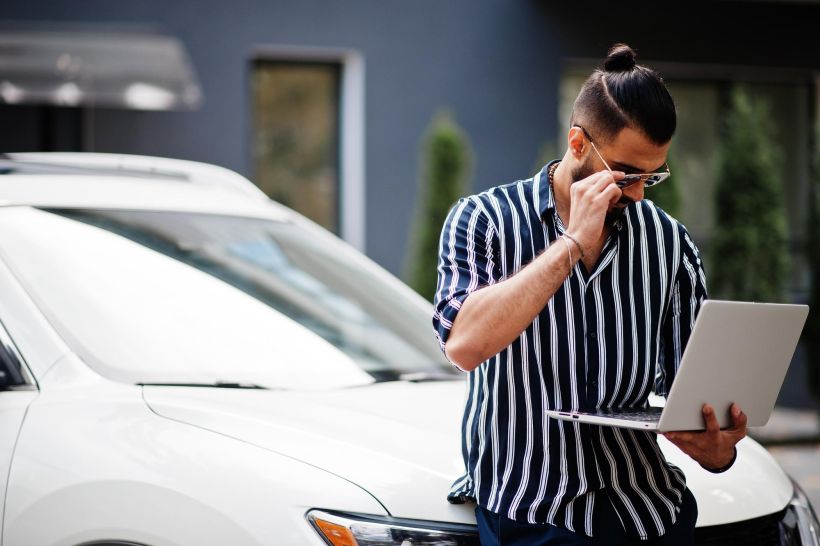 Hombre exitoso vestido con camisa a rayas y gafas de sol mirando su ordenador port&aacute;til con un bonito mensaje.