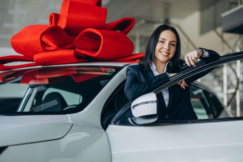 Young woman near a car with a large red bow.