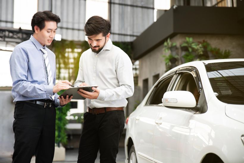 Un joven firma documentos junto a un coche.