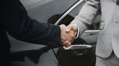 Two men shake hands by a car, finalizing the transfer of a car title in California
