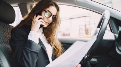 A woman in her car makes a phone call while reviewing documents for a salvage title California