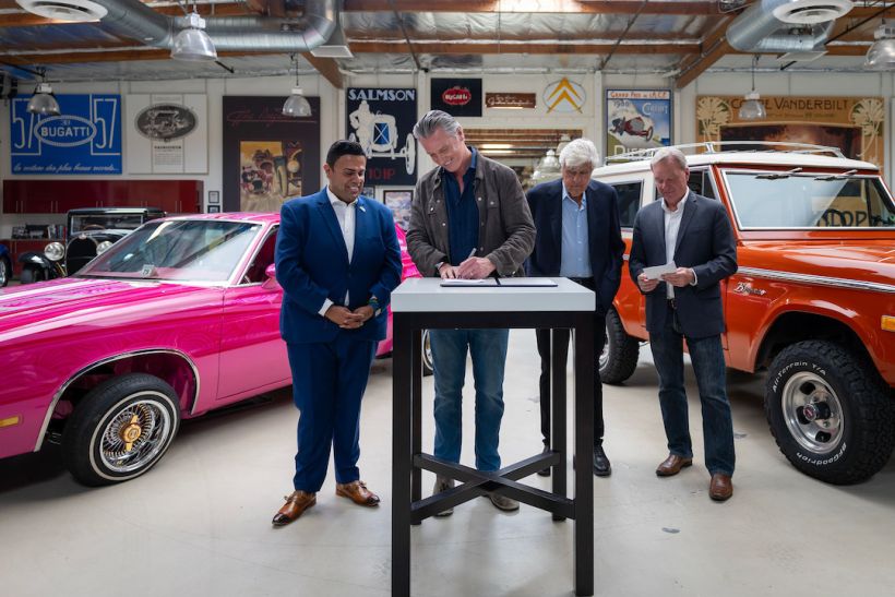 El gobernador Newsom y Jay Leno de pie juntos en un gran garaje privado