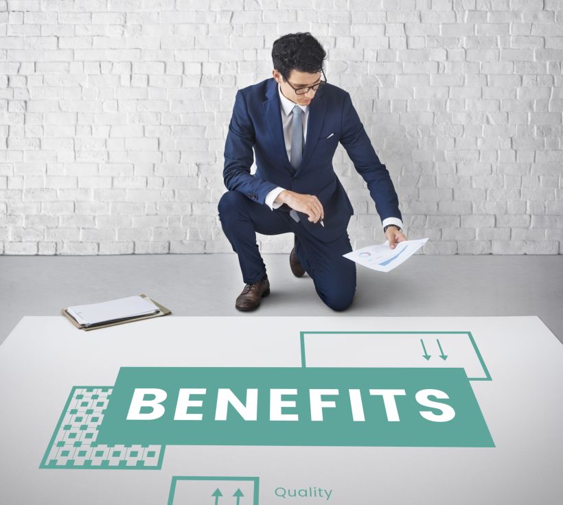 A young man stands next to a sign with the word &ldquo;benefits&rdquo; written on it.